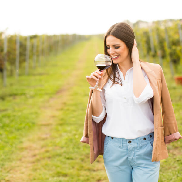 Una mujer sostiene una copa de vino en un viñedo, rodeada de uvas y paisajes de los mejores viñedos