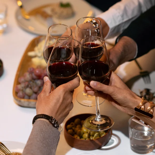 Un grupo de personas brindando con copas de vino en un ambiente festivo, disfrutando de vino y comida.