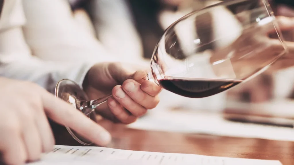 Persona sosteniendo una copa de vino sobre un papel relacionado con la enología.