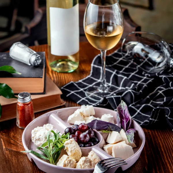 Un plato con queso, uvas y una copa de vino sobre una mesa, representando una experiencia de vino y comida.